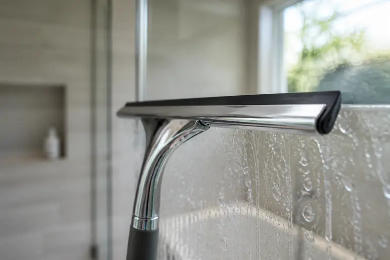 Éviter calcaire vitre douche : raclette propre sur paroi de douche après usage