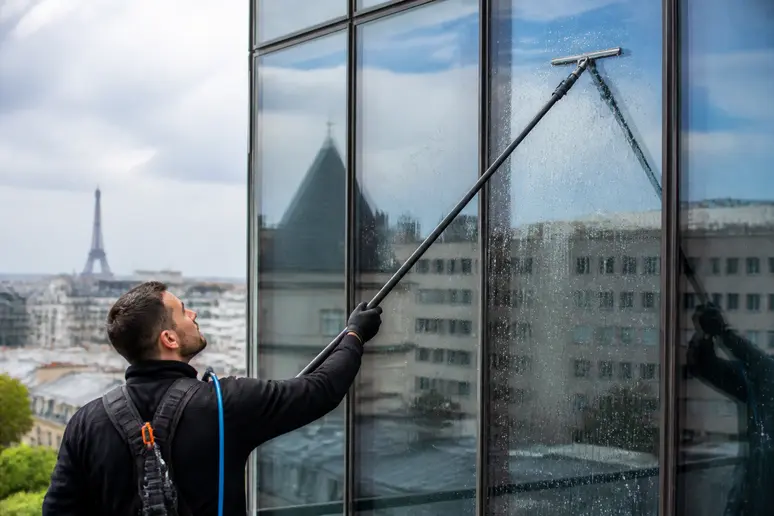 Professionnel nettoyant une large façade vitrée avec une perche télescopique, nettoyeur vitre professionnel.