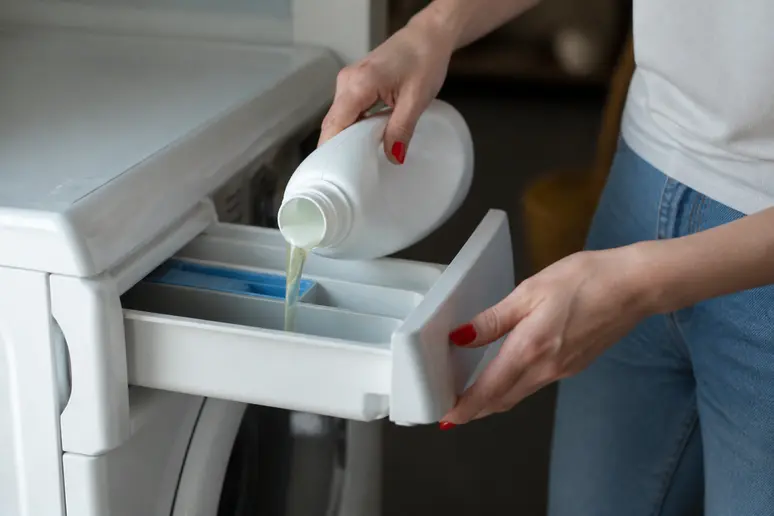 Main utilisant un produit anti odeur machine à laver dans le compartiment à lessive.
