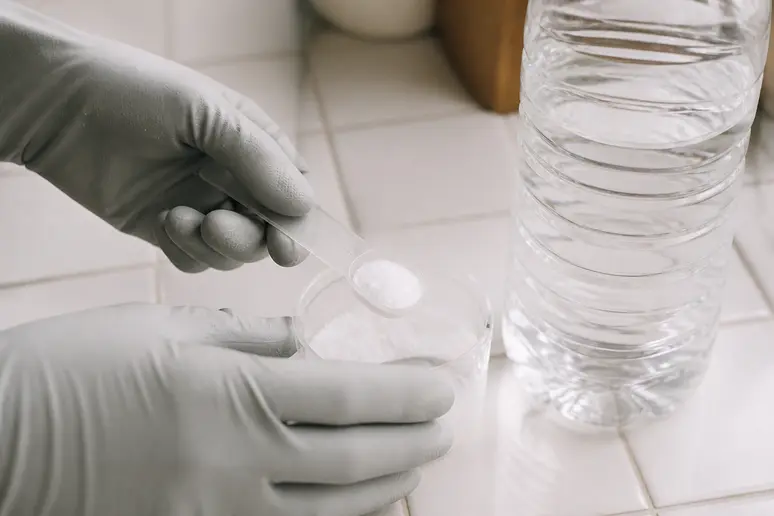 Main gantée manipulant des cristaux de soude, un produit joint carrelage puissant pour les taches tenaces.
