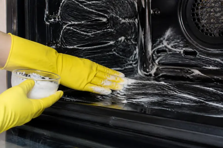 Application méticuleuse d'une pâte de bicarbonate de soude pour le nettoyage du four.