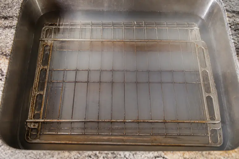 Grilles de four trempant dans une eau chaude au bicarbonate de soude pour un nettoyage profond.