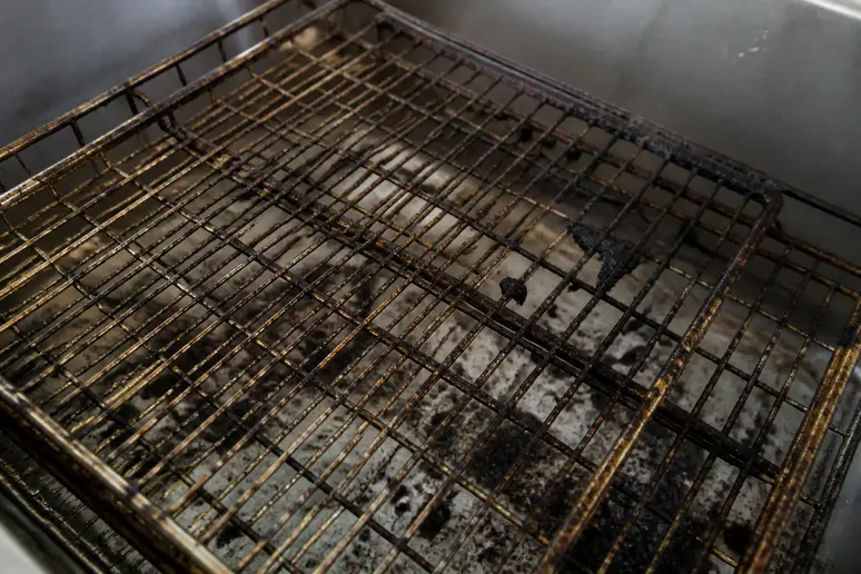 Vue rapprochée de grilles de four très encrassées, montrant les dépôts de graisse carbonisée et résidus alimentaires, un exemple de ce qu'implique comment nettoyer un four très encrassé.
