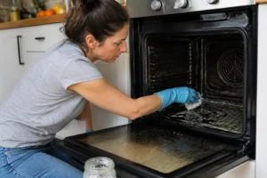 Femme nettoyant un four très encrassé avec une pâte naturelle dans sa cuisine.