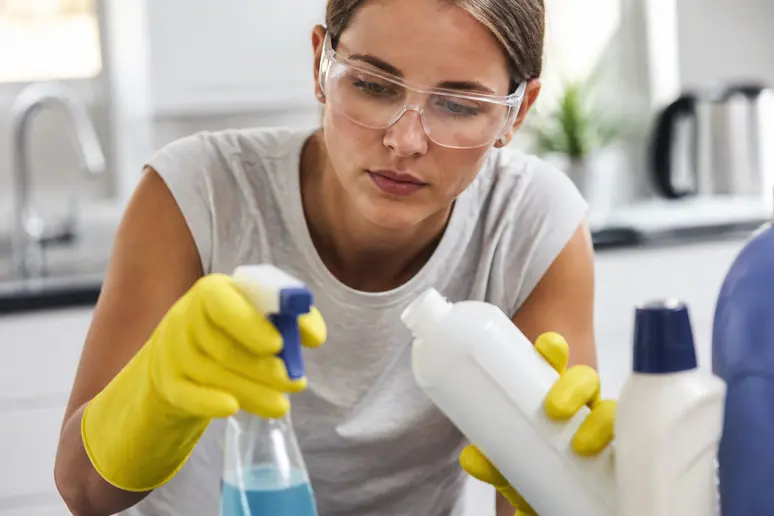 Personne portant des gants de protection et des lunettes pour manipuler des produits d'entretien