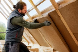 artisan posant des panneaux d'isolation naturelle en fibre de bois sous les rampants d'une toiture