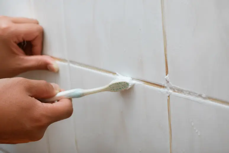 Application d'une pâte nettoyante sur des joints de douche noircis avec une brosse.