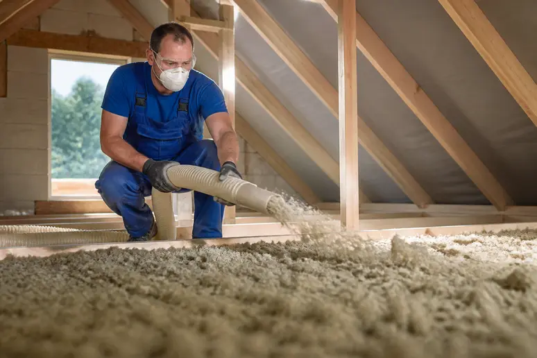 Soufflage de laine de roche sur le plancher de combles perdus par un professionnel.