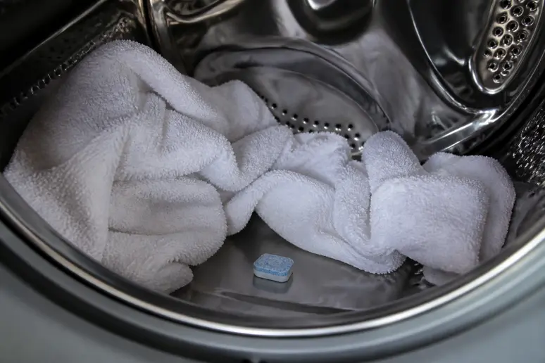 Une tablette d'anti-calcaire au fond du tambour avec du linge blanc.
