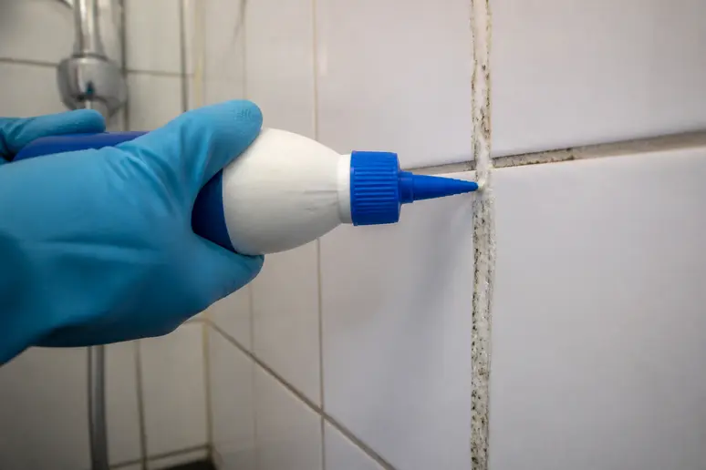 Application précise d'un gel nettoyant sur les joints de carrelage verticaux d'une douche