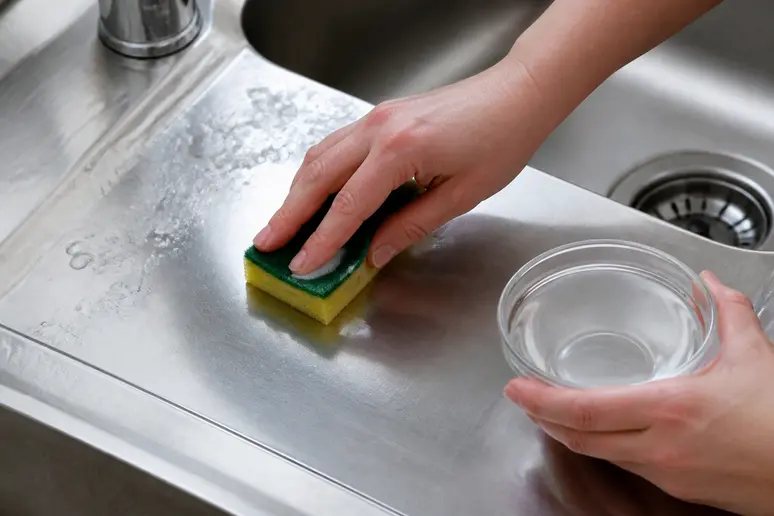 Main appliquant un produit pour nettoyer inox avec du vinaigre blanc dilué sur un évier.