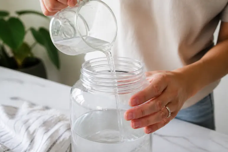 Main versant du vinaigre blanc dans de l'eau chaude pour un produit vitre maison.