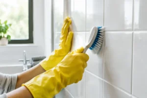 Une personne en gants de ménage frotte soigneusement les carreaux pour blanchir joint douche.