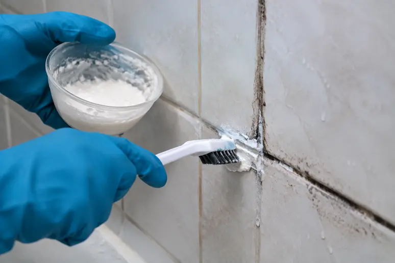 Mains gantées appliquant une pâte au bicarbonate pour enlever la moisissure du joint de carrelage