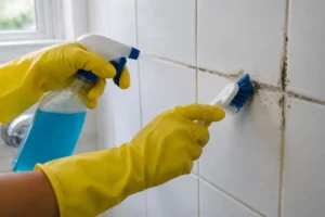 Personne en gants jaunes utilisant une brosse pour enlever moisissure joint de carrelage dans une salle de bain