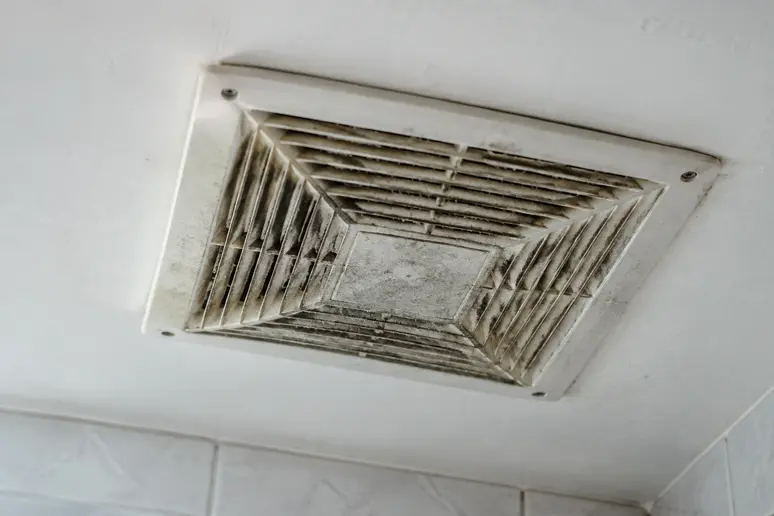 Bouche d'extraction VMC encrassée accumulant de la poussière au plafond d'une pièce humide.