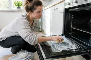 Une personne applique une pâte de bicarbonate sur la vitre pour nettoyer four vinaigre blanc bicarbonate.