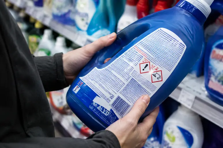 Mains lisant les pictogrammes de danger sur l'étiquette d'un produit lave-linge en magasin