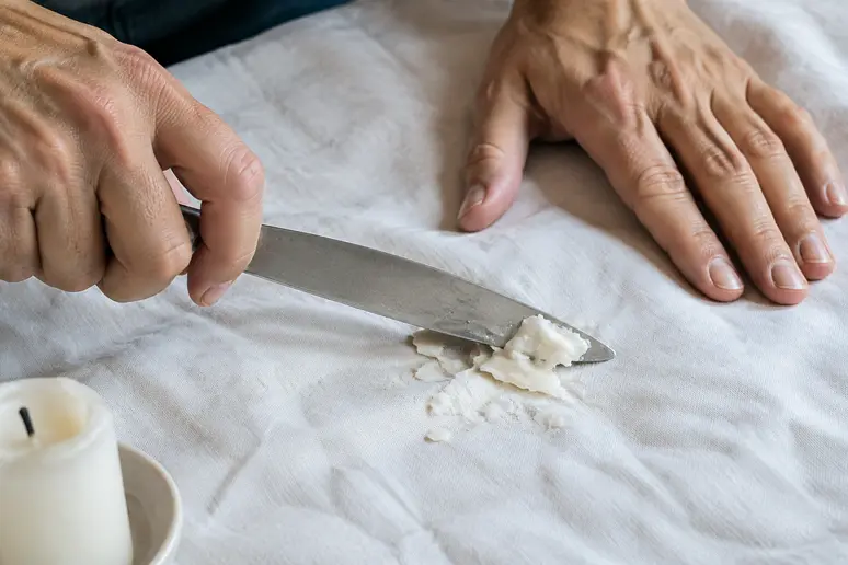 Mains grattant délicatement de la cire de bougie froide sur une nappe avec un couteau