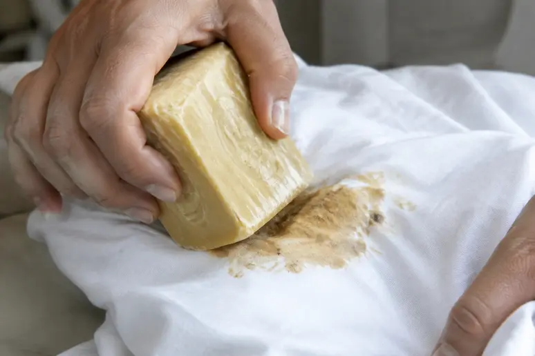 Application d'un bloc de savon de Marseille sec sur une trace de gras sur un pantalon blanc