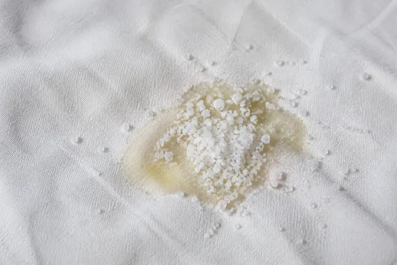 Gros plan de sel fin posé sur une tache de graisse fraîche sur un vêtement blanc